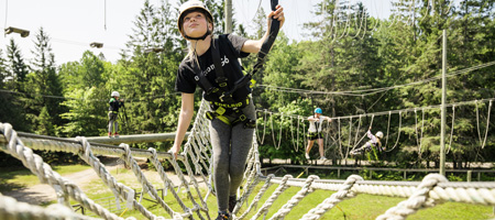 Une jeune adolescente traverse un pont de corde étroit.